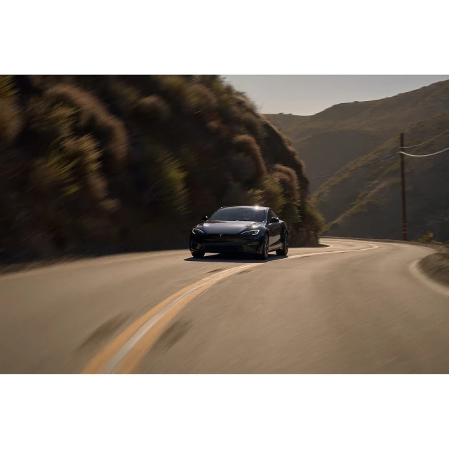Black electric car drives on a winding road through mountainous landscape on a sunny day with blurred motion, cinematic color grading.