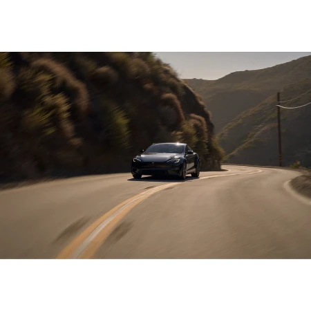 Black electric car drives on a winding road through mountainous landscape on a sunny day with blurred motion, cinematic color grading.