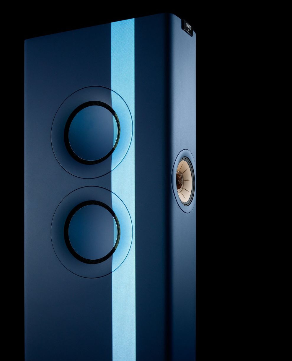 Close-up of a modern floor-standing loudspeaker in matte blue, featuring circular sound-generating units and a vertical light stripe.