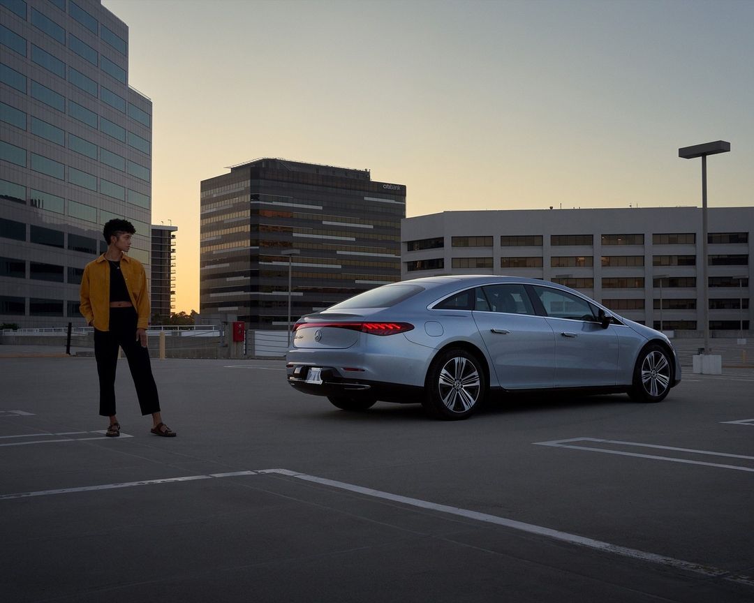 Silver car parked on a rooftop with an adult standing nearby, set against an urban skyline at dusk.