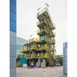 Tall industrial processing tower with yellow staircases and platforms outdoors by Greg White