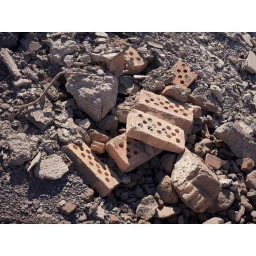 Scattered rubble including perforated red clay bricks and broken concrete pieces on a dusty ground.