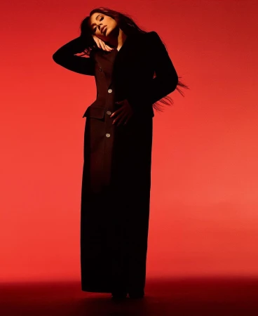 Woman wearing a dark structured blazer and long skirt posing against a vibrant red backdrop in New York.