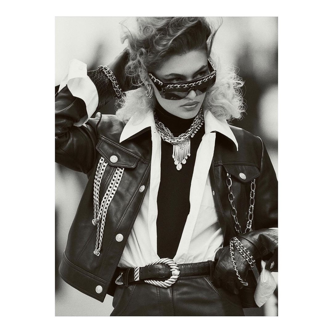 Black and white editorial portrait of a woman wearing leather jacket, chain-embellished sunglasses, and layered necklaces by Gregory Harris.
