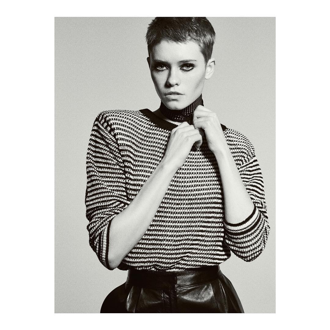 Monochrome portrait of a woman with short hair wearing a striped sweater and leather skirt against a plain background.