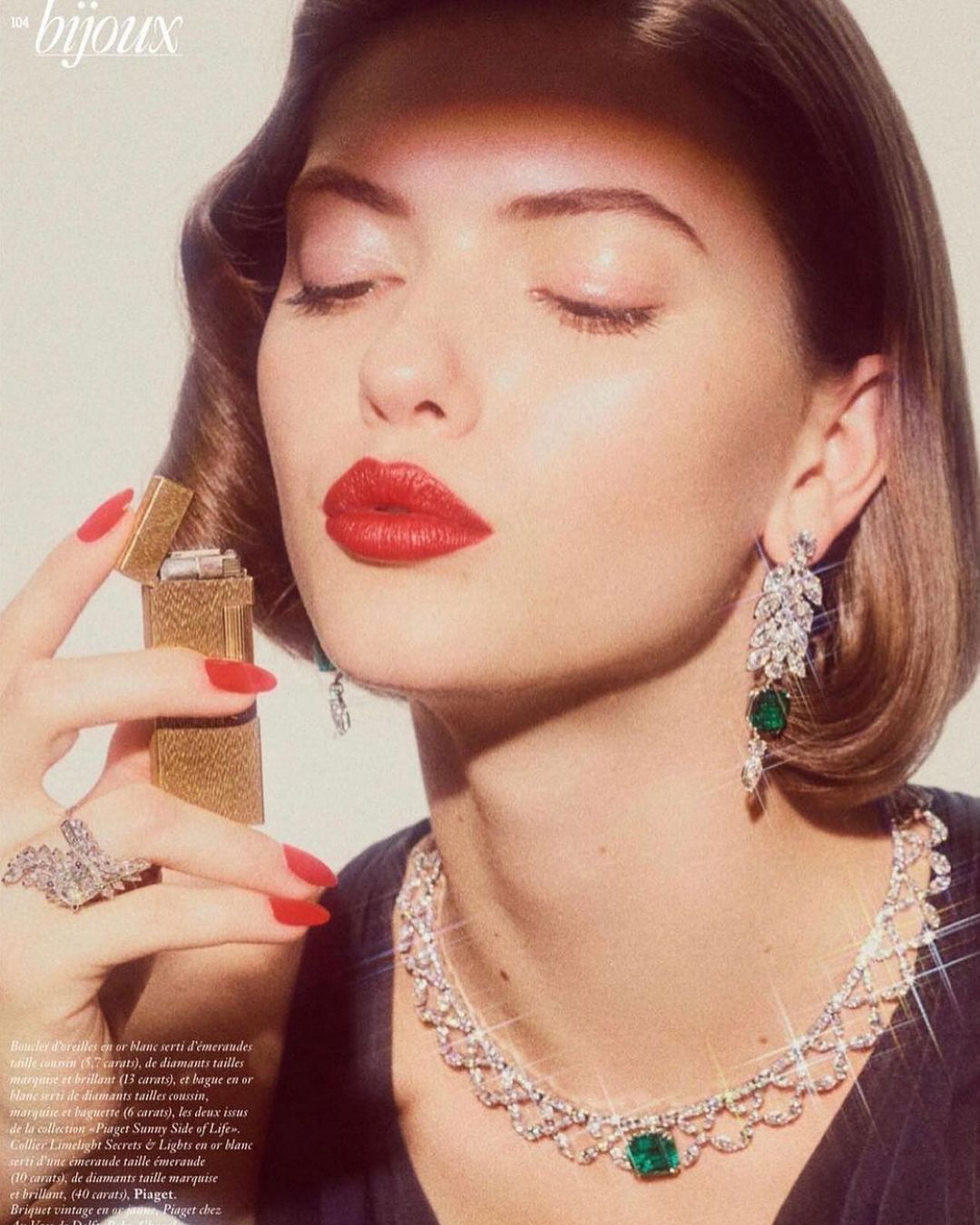 Elegant woman with red lipstick poses with vintage jewelry and a gold lighter. Studio lighting highlights the glamorous fashion aesthetic.