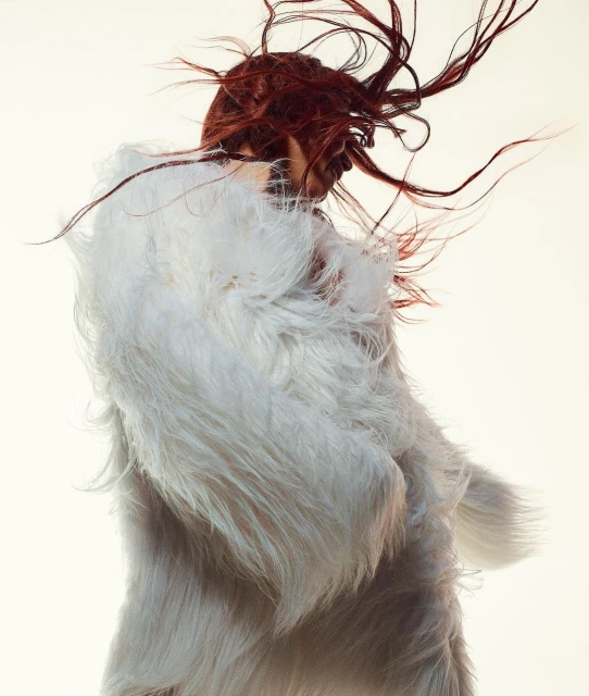 Woman in a white faux fur coat with flowing red hair against a bright white background. Fashion photography.