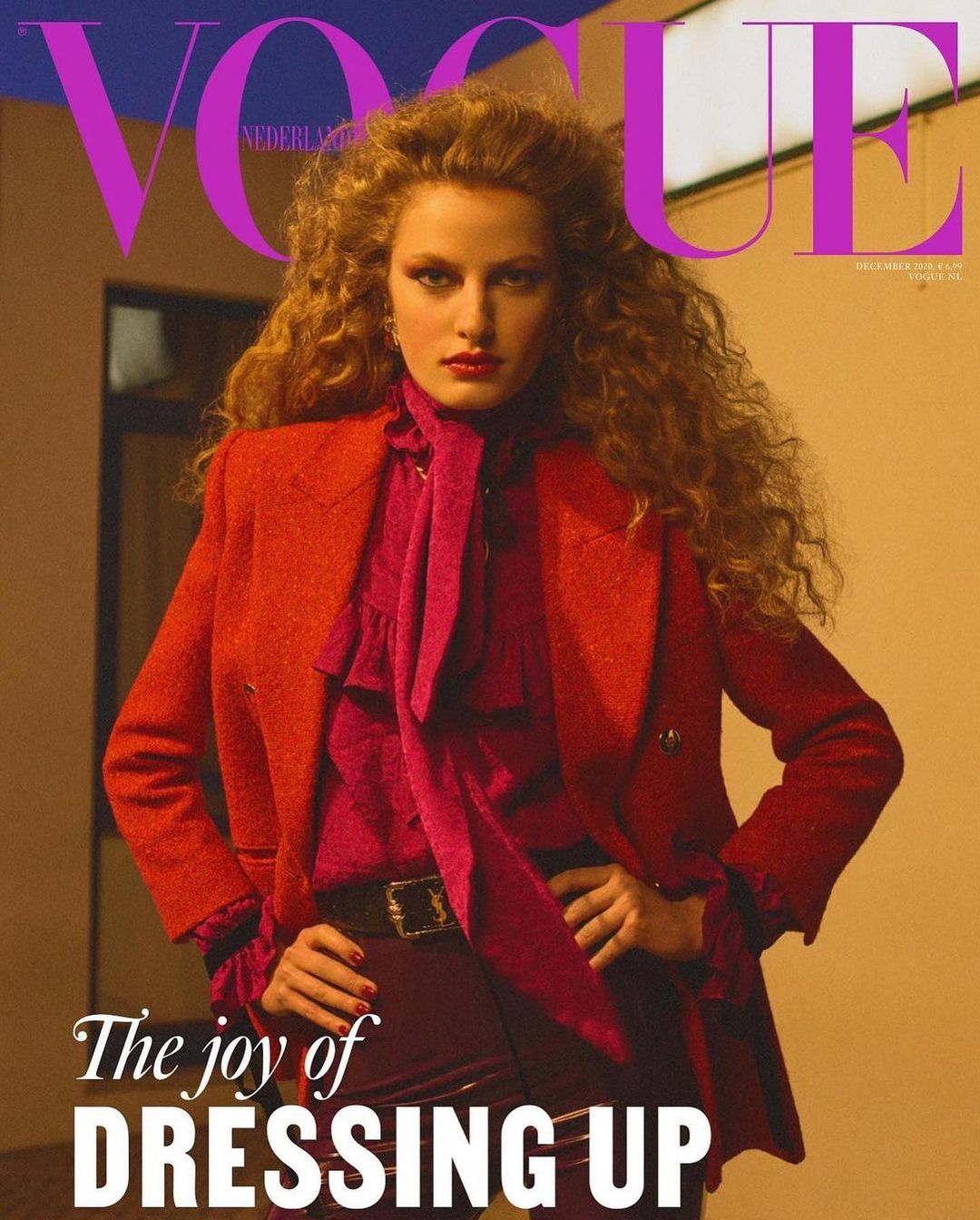 Vogue Nederland cover featuring a woman with curly red hair wearing an orange blazer, pink blouse, and maroon pants. Fashion editorial.