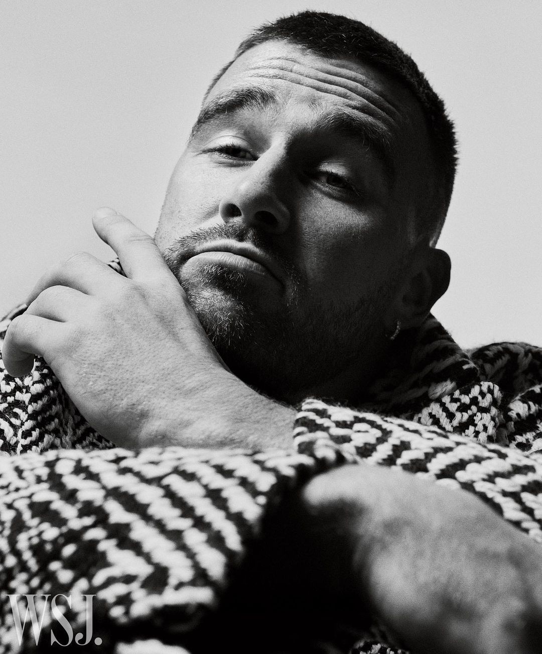 Close up portrait of man with short hair wearing patterned jacket resting chin on hand by Gregory Harris