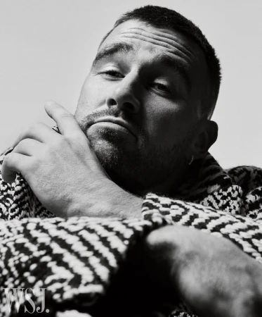 Close up portrait of man with short hair wearing patterned jacket resting chin on hand by Gregory Harris