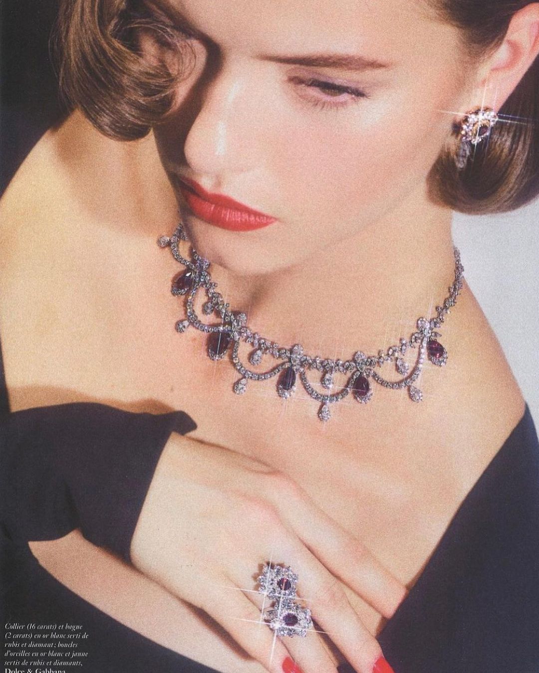 A woman with red lipstick is featured wearing a silver necklace, ring, and earrings with dark purple stones in a close-up shot.