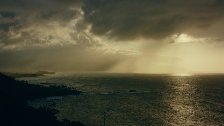 Coastal view of the ocean under an overcast sky, featuring sunlight breaking through the clouds and reflecting on the water's surface.