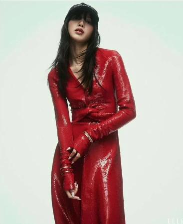 Woman in shiny red dress and black cap posing in photo studio, portrait orientation, fashion editorial, neutral expression. 
