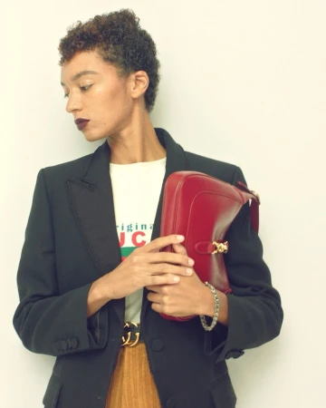 Model with short curly brown hair wearing a black blazer and holding a red handbag by photographer Gregory Harris