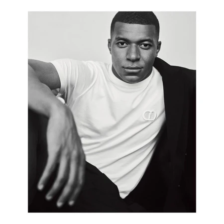 Kylian Mbappé wearing a white t-shirt and dark jacket against a plain background in a portrait photograph by Gregory Harris.
