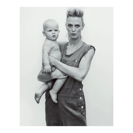 Woman in overalls holding a baby against a plain light background photographed in New York by Gregory Harris