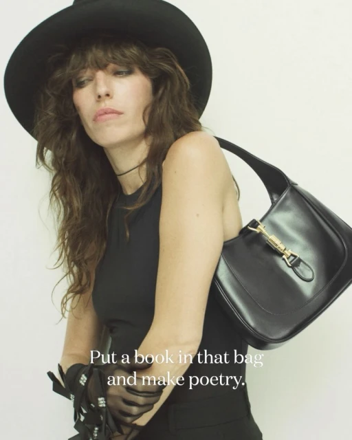 A woman in a black hat poses with a black leather purse in a studio setting, showcasing fashion and style.