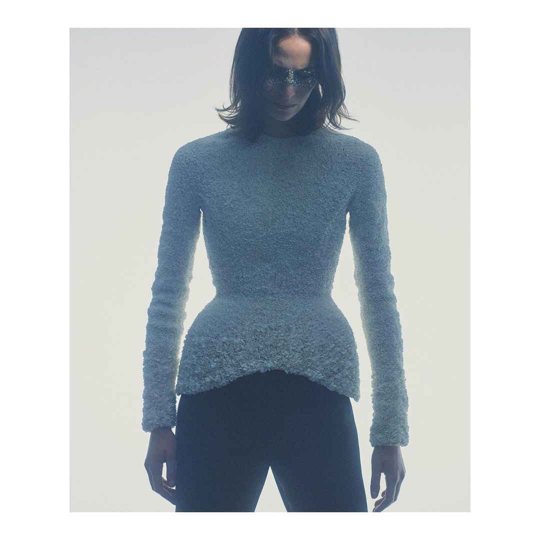 Model in textured light blue long-sleeve top and dark trousers against white background by Gregory Harris