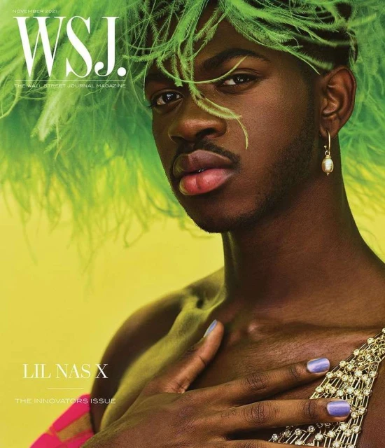Magazine cover featuring Lil Nas X, adorned with green feathers, lilac nails, and jeweled attire, against a yellow background.