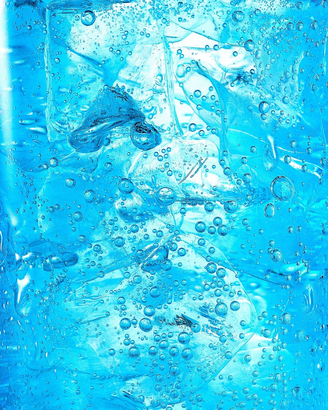 Close-up studio shot of a glass filled with ice cubes and a blue liquid, showcasing condensation and bubbles.
