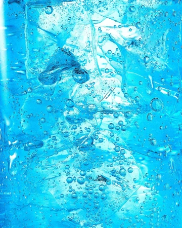 Close-up of bright blue carbonated drink filled with clear ice cubes and rising bubbles by Gregory Reid.