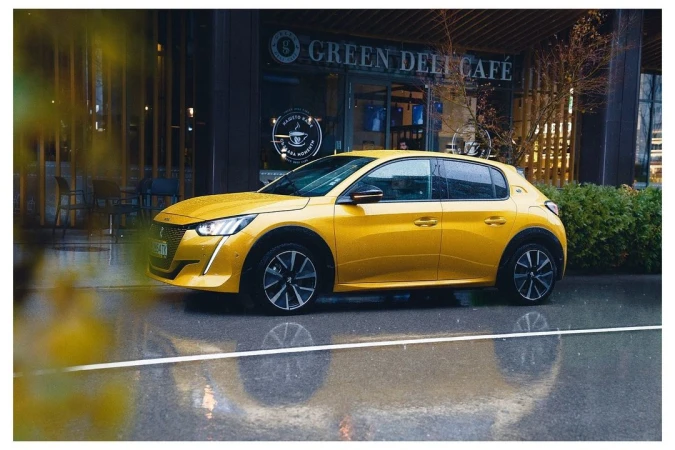 A yellow Peugeot 208 hatchback car is parked outside the Green Deli Cafe with wet asphalt reflecting the vehicle's form and light.