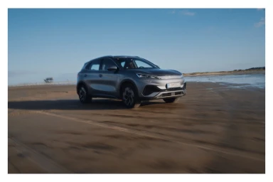 Silver electric SUV driving along a wet sandy beach under a clear blue sky