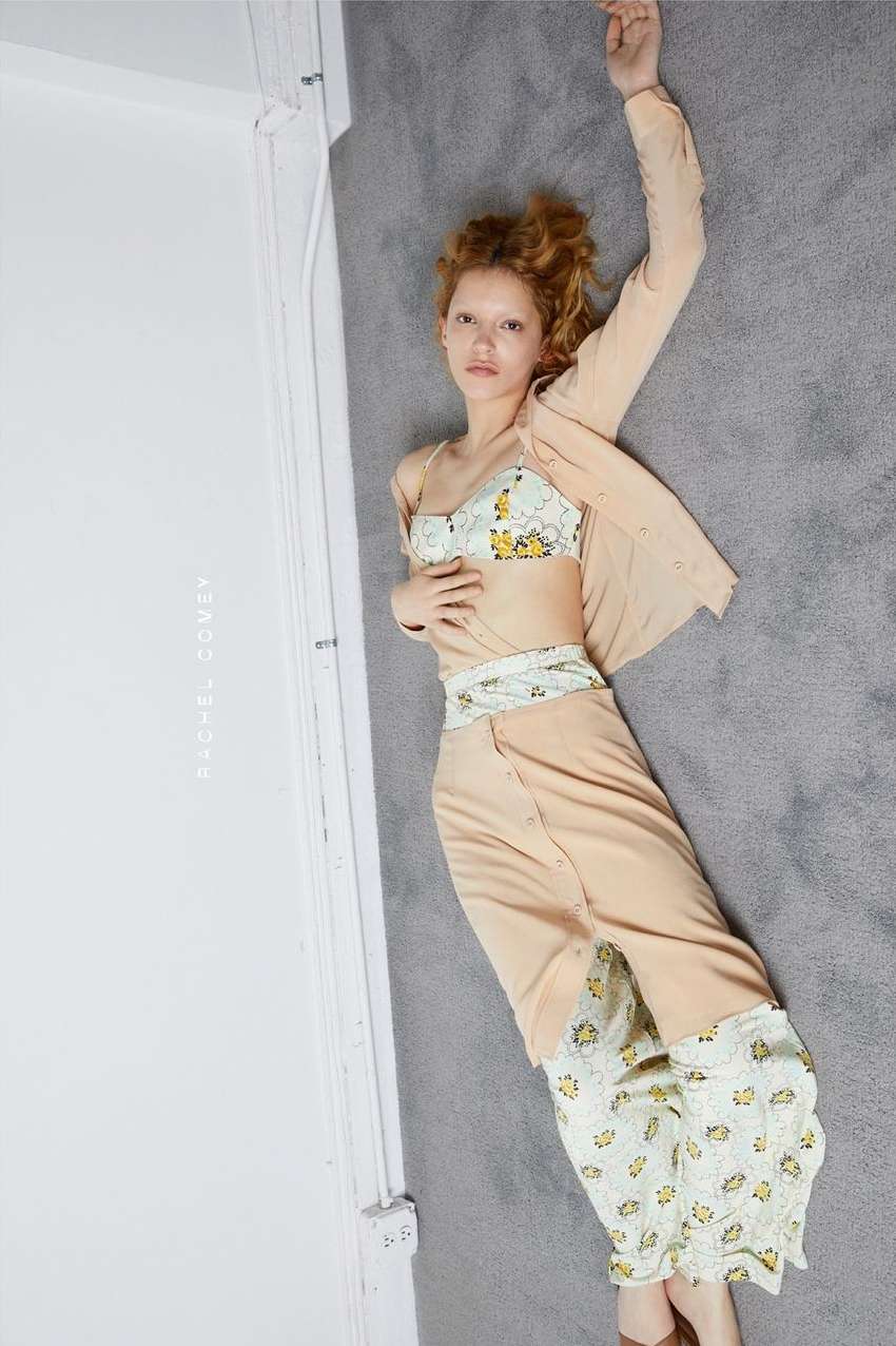 Overhead shot of a woman lying on a gray rug in a light peach two piece floral outfit in a bright studio with white walls.