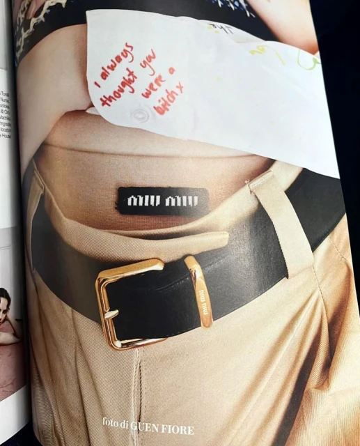 Fashion magazine page with a close-up of a woman's waist and black belt with a gold buckle and a handwritten note.