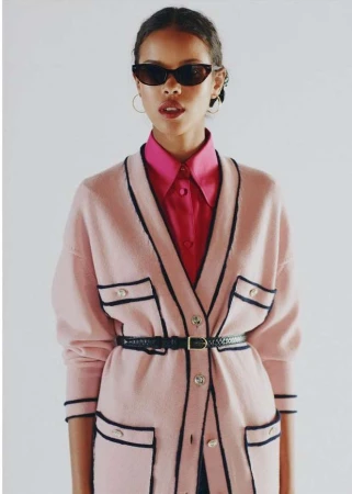 Woman in pink cardigan and sunglasses poses in a studio portrait, showcasing fashion and style against a clean white backdrop.