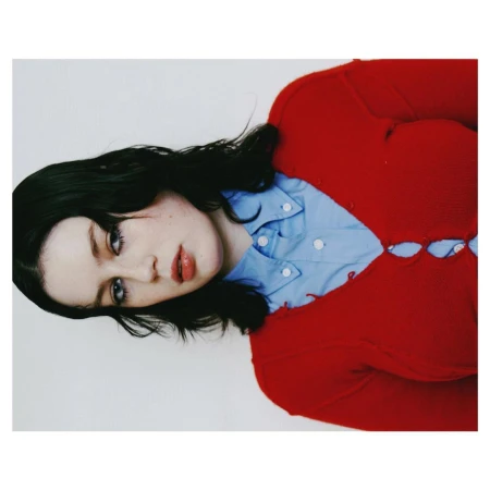 Portrait of a woman wearing a red cardigan and light blue button-down shirt against a white seamless backdrop.