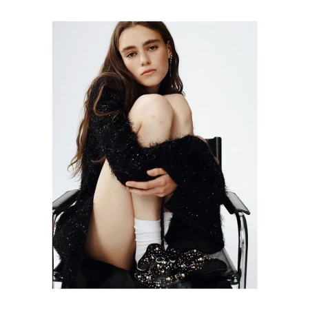 Adult female posing in a black cardigan while sitting on a black chair in front of a white background in a studio environment.