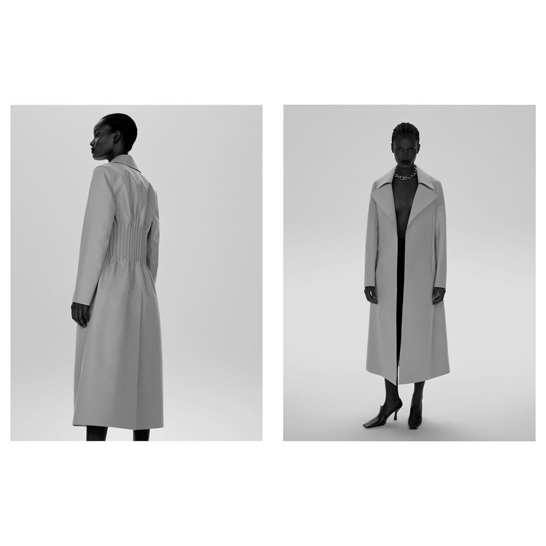 Two views of a black female model wearing a long grey trench coat, square-toe heels, and a silver necklace against a studio backdrop.