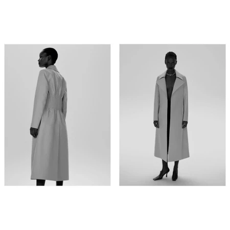 Two views of a black female model wearing a long grey trench coat, square-toe heels, and a silver necklace against a studio backdrop.