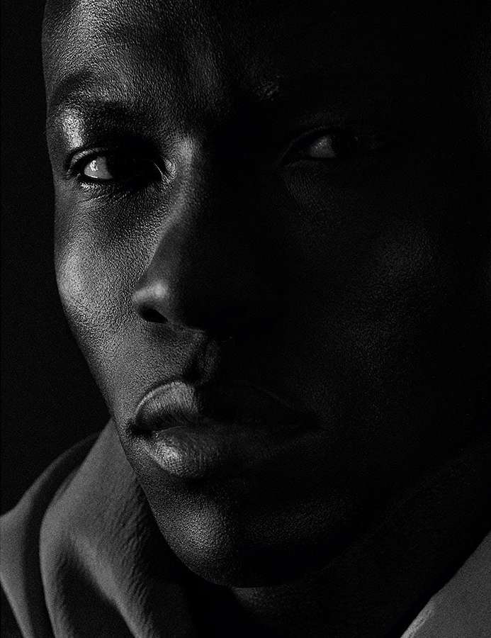 Portrait of an African American man with dark skin and a serious expression, captured with dramatic lighting and a black and white filter.