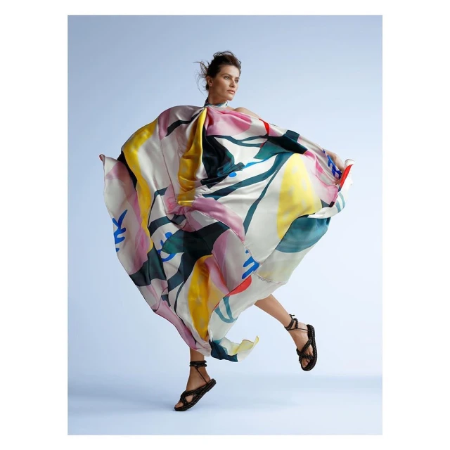 Woman in a vibrant, flowing dress leaps gracefully in a light blue studio, showcasing fashion and style with a blend of art and motion.