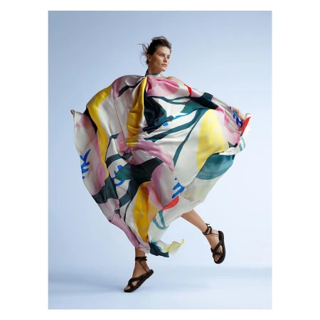 Woman in a vibrant, flowing dress leaps gracefully in a light blue studio, showcasing fashion and style with a blend of art and motion.