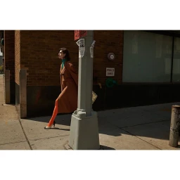Woman in brown coat and bright orange tights walking on a city sidewalk next to a brick building.