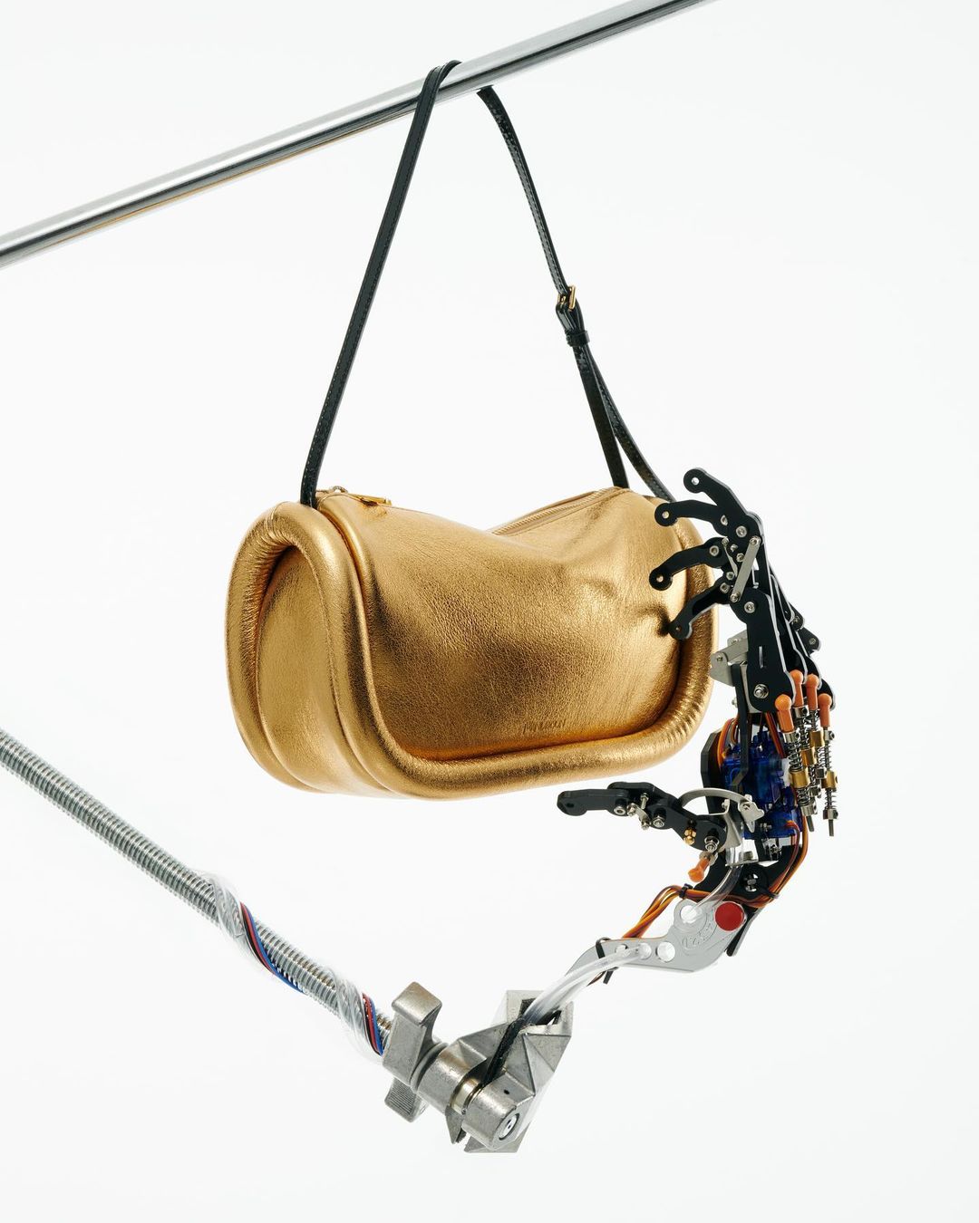 Gold purse held by a robotic arm against a white background. Close-up studio shot highlights the textures and contrasting elements.