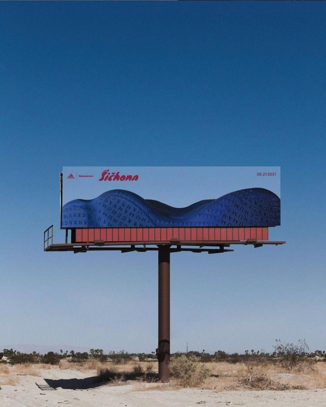 Outdoor billboard featuring an abstract design with blue hues and the Adidas logo against a clear blue sky and desert landscape.