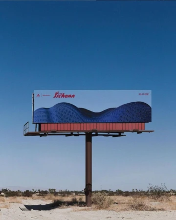 Outdoor billboard featuring an abstract design with blue hues and the Adidas logo against a clear blue sky and desert landscape.