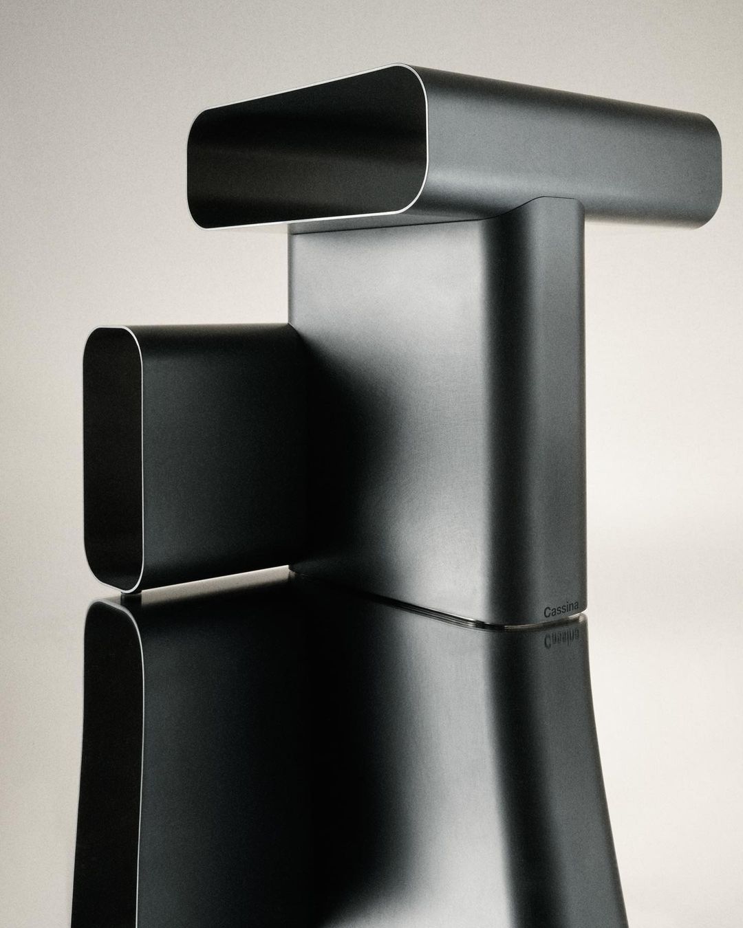 Modernist black metal sculpture on reflective surface. Architectural design of curving, tubular metal shapes in a neutral light.