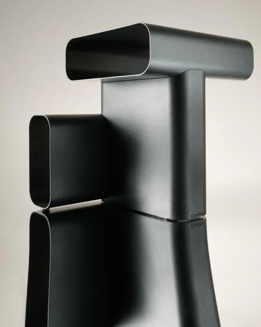 Modernist black metal sculpture on reflective surface. Architectural design of curving, tubular metal shapes in a neutral light.