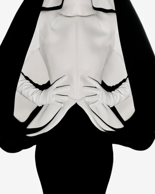 Elegant upper-body fashion portrait with a model wearing a white jacket, gloves, and a black dress against a bright background.
