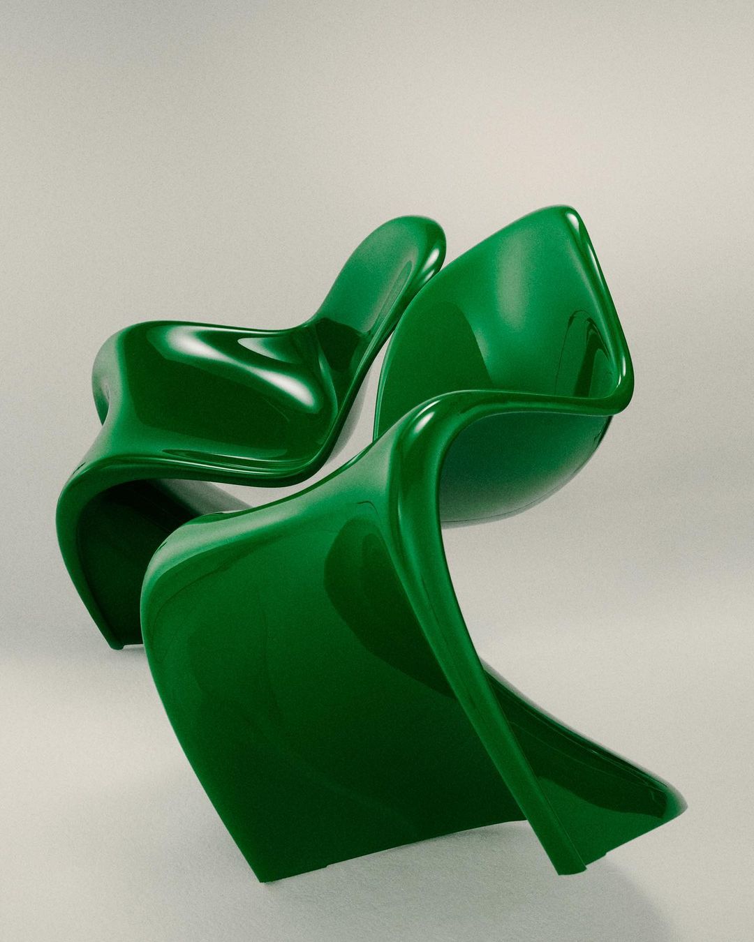 Modern green plastic chairs with curving shapes sit in front of a neutral background in a studio setting. Contemporary furniture design.