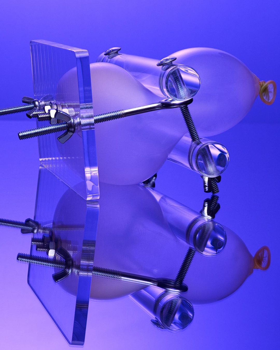 Abstract shot of balloons held in clear plastic apparatus on a graduated blue background with reflection in a product photography setting.