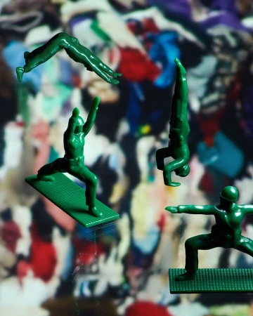 A group of green plastic toy soldiers in various yoga poses against a blurred colorful background suggesting physical fitness and play.
