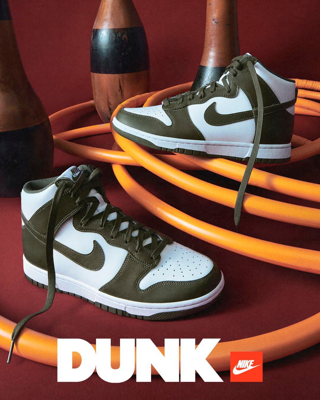 Nike Dunk High sneakers in white and olive green, with bowling pins and orange tubing in a studio product shot for Visie.