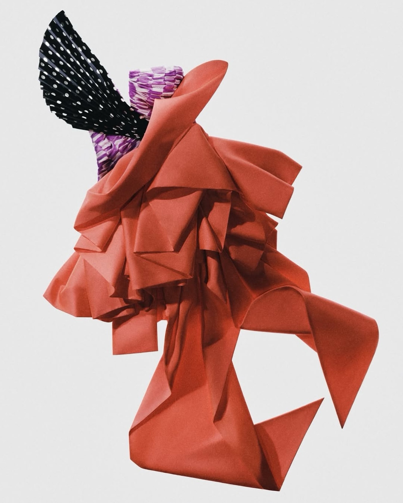 Abstract fabric art features coral draping, purple patterned column, and black and white polka dot fan against a plain background.
