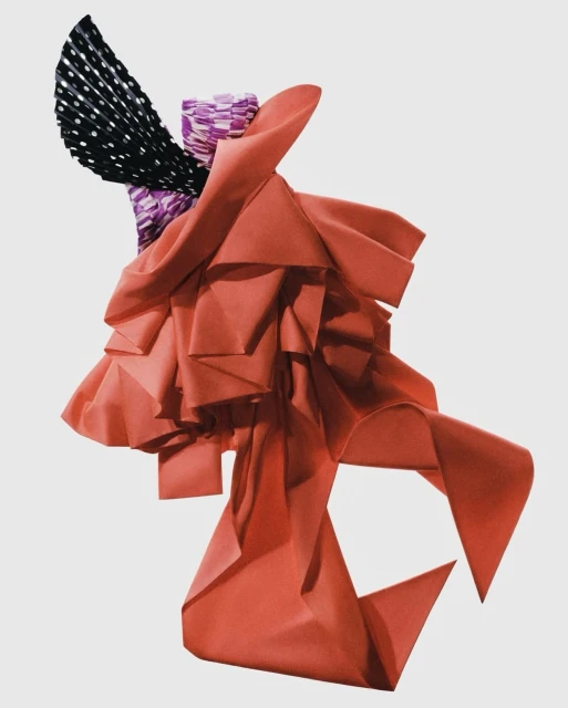 Abstract fabric art features coral draping, purple patterned column, and black and white polka dot fan against a plain background.